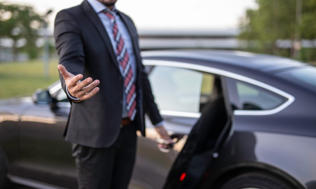 Handsome young man chauffeur holding a door and reaching out hand to help